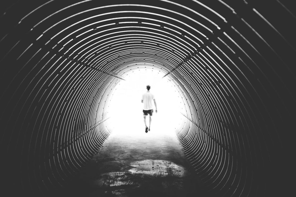 Man walking toward bright light at the end of a tunnel, symbolizing searching for direction and finding purpose as a man.