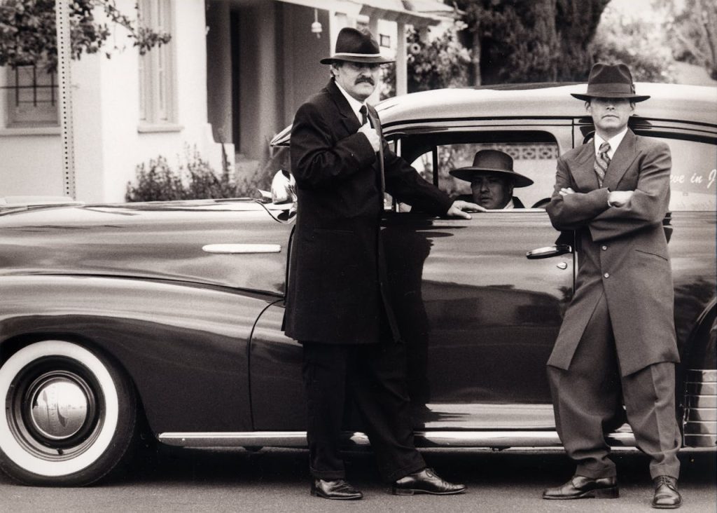 Three men in vintage 1950s attire standing beside a classic car, embodying traditional masculine stoicism and emotional distance.