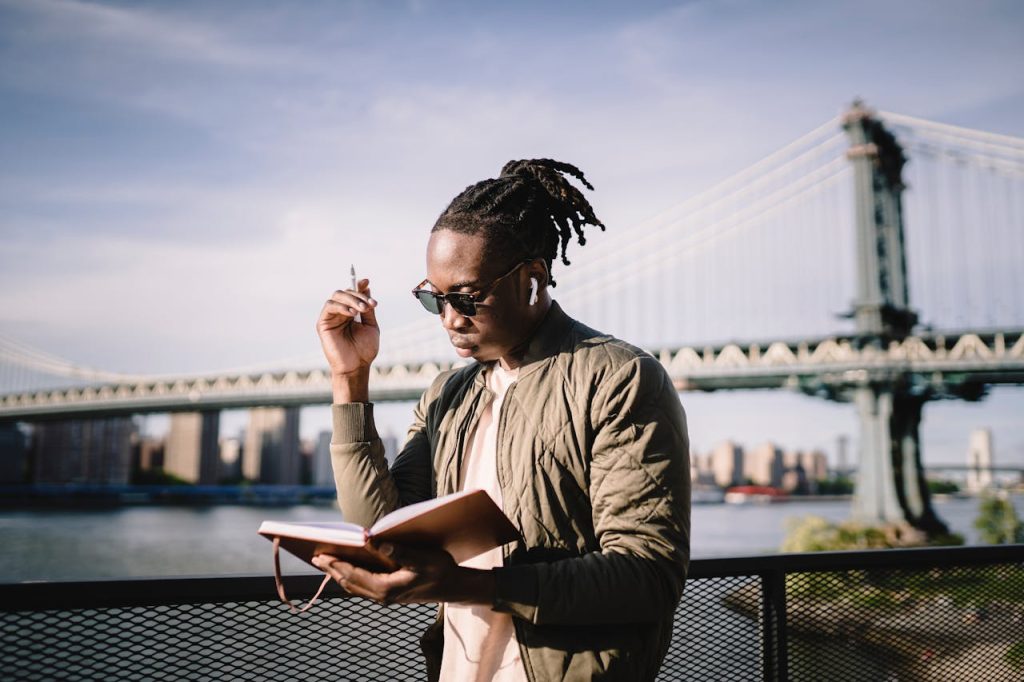 A man journaling outdoors near a city bridge, reflecting thoughtfully as he writes, symbolizing self-discovery and personal growth.