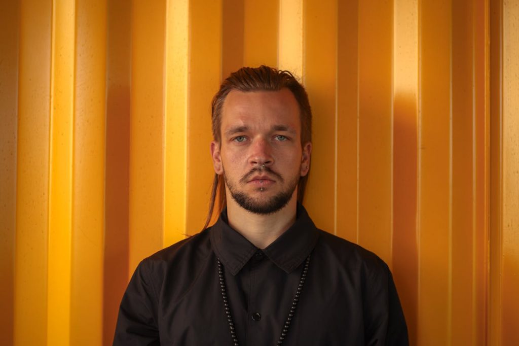 Man with a blank, emotionless expression standing against a yellow wall, illustrating men and emotional numbness.
