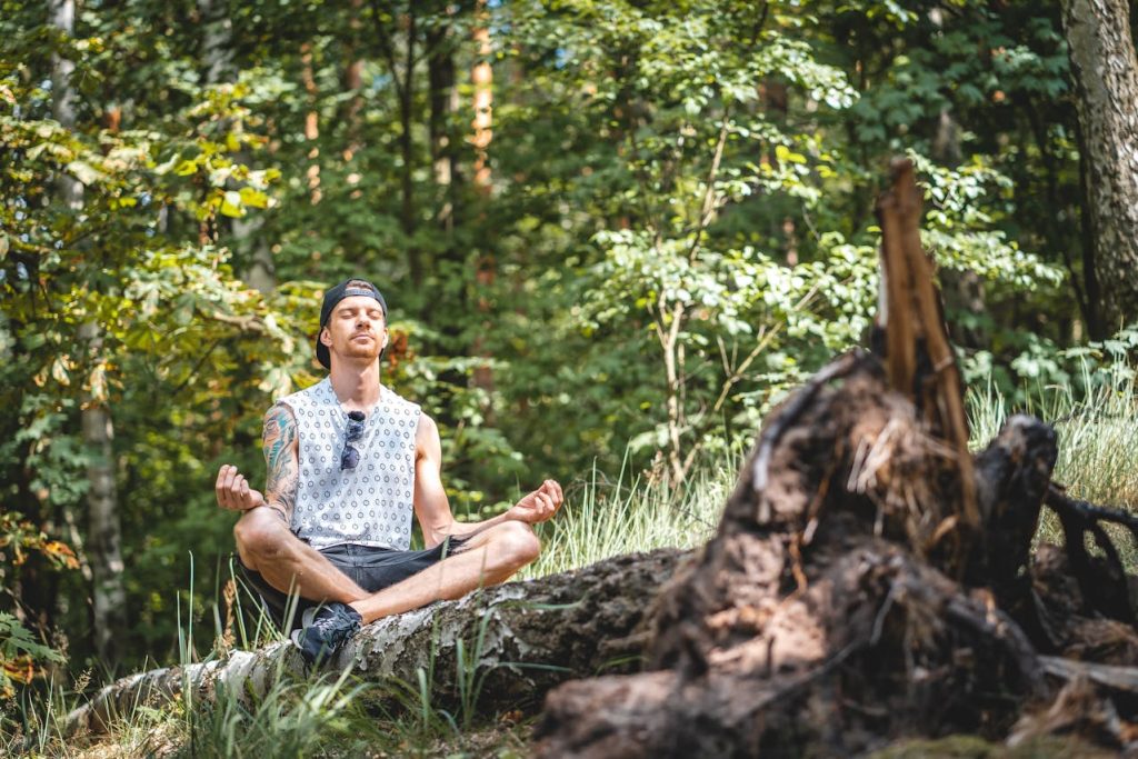 Man meditating outdoors in a forest, sitting cross-legged with closed eyes, demonstrating mental strength, focus, and emotional regulation.