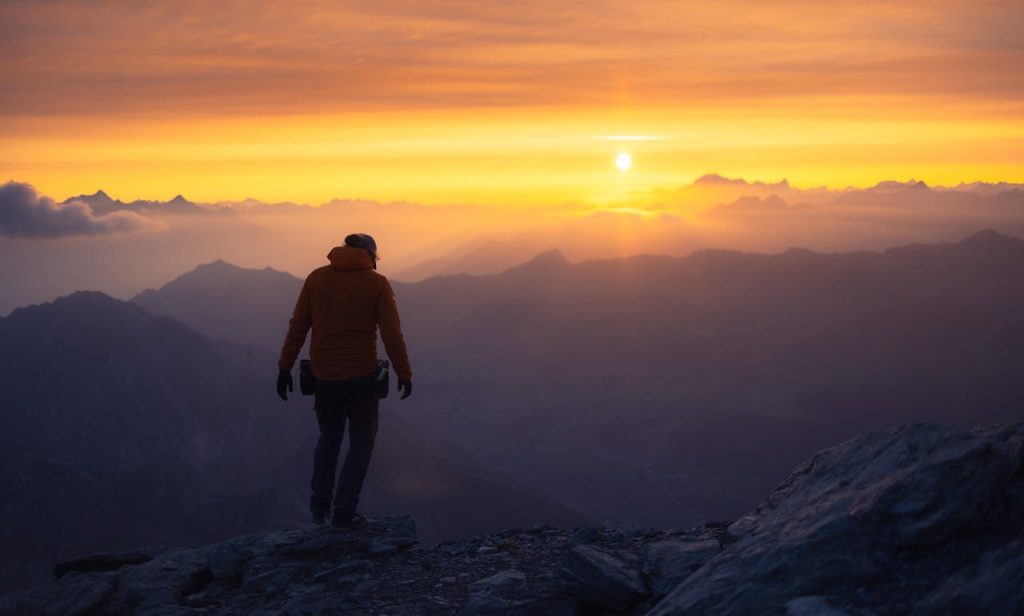 Person walking toward a glowing sunrise on a mountain ridge, symbolizing new beginnings, healing, and emotional transformation.