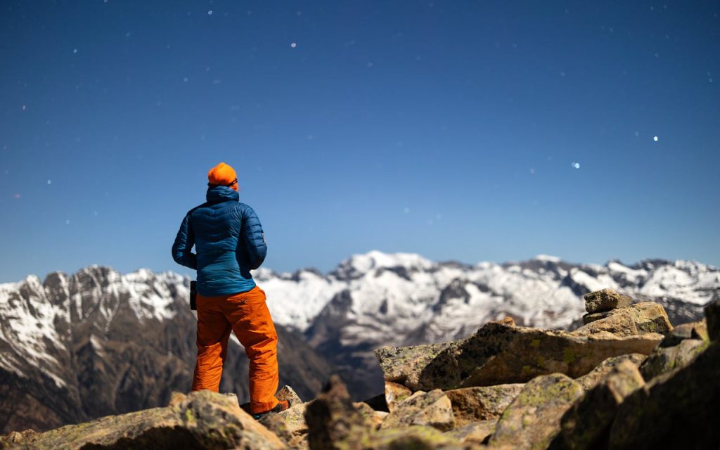 Man standing on a mountain peak at sunrise, looking out over snowy cliffs, symbolizing clarity, freedom, and the strength that comes from living authentically.