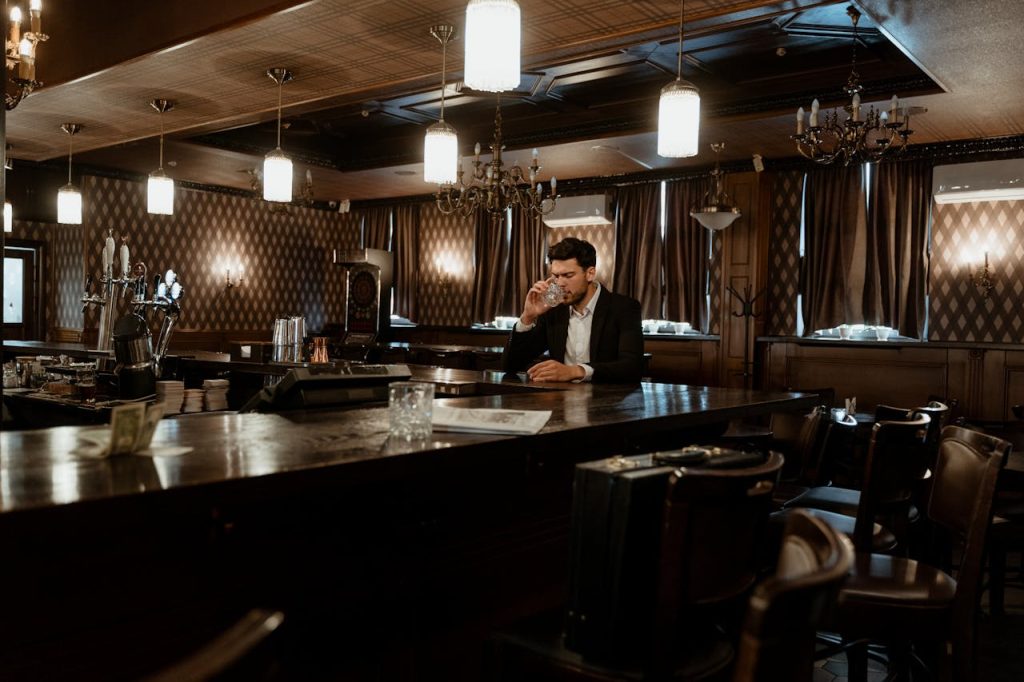 A man sitting alone at a bar with a drink, appearing distant and withdrawn, illustrating avoidant attachment in men through emotional disengagement and isolation.