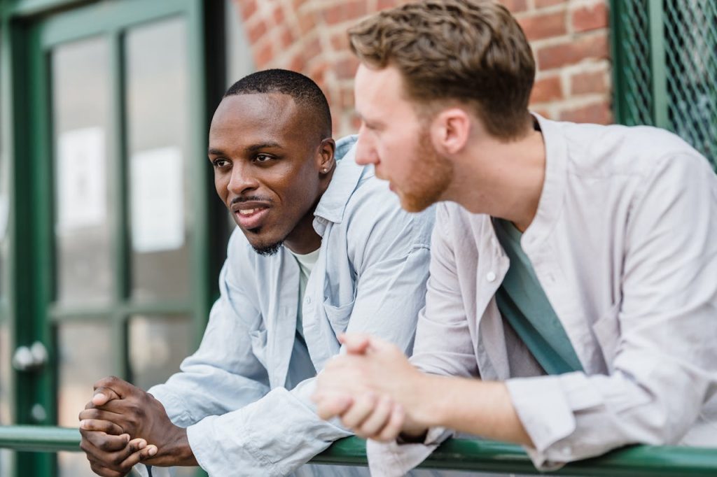 Two men talking openly outdoors, with one man expressing vulnerability while confidently seeking support from a trusted friend.