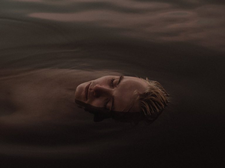 A man floating peacefully in calm water with eyes closed, symbolizing self-forgiveness, release of guilt, and emotional healing.
