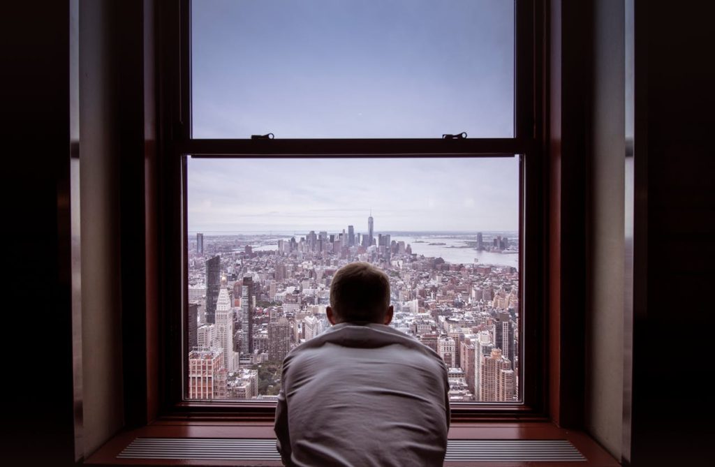 Man looking out a large window over a city skyline, symbolizing healthy boundaries that protect while still allowing openness and connection.