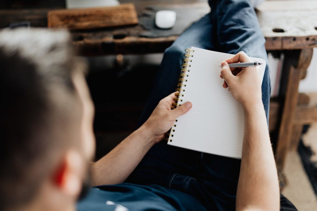Man journaling in a notebook at a desk with soft natural lighting.