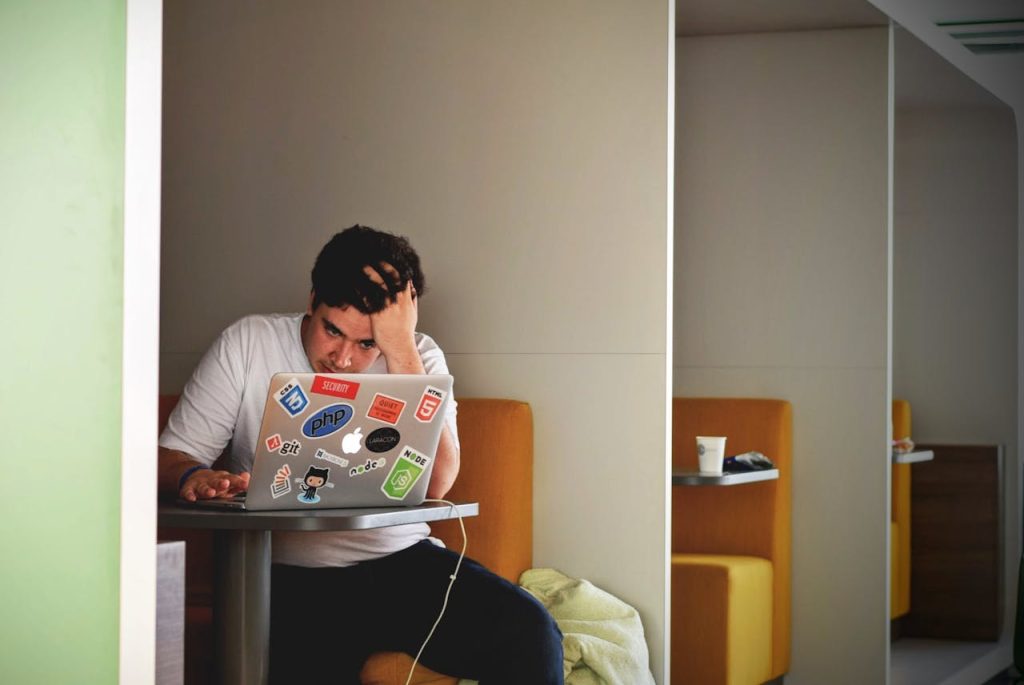 A man sitting alone with a laptop, looking stressed and overwhelmed, illustrating Nice Guy syndrome through internal pressure, people-pleasing, and suppressed resentment.