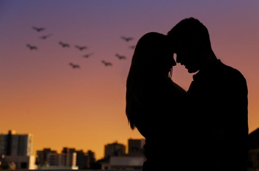 A couple in silhouette leaning into each other at sunset, symbolizing secure emotional connection, presence, and mutual attunement in a healthy relationship.