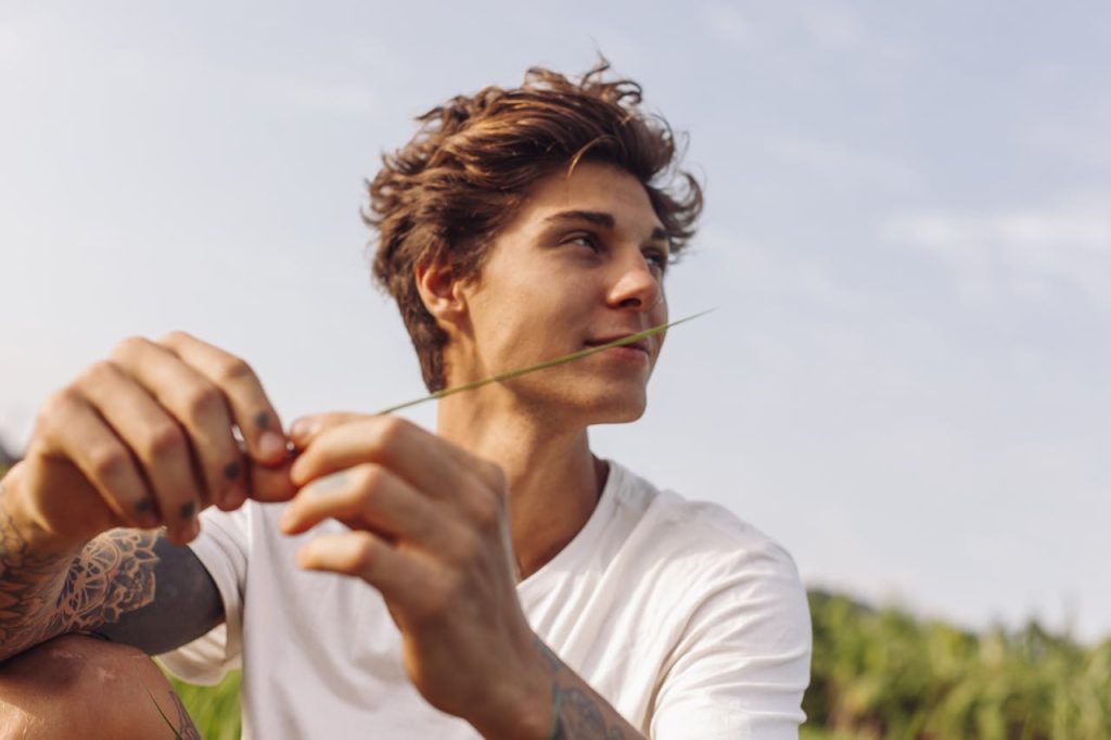 Young man relaxing outdoors and showing a calm, reflective expression, symbolizing healthy emotional expression appropriate to personal contexts.