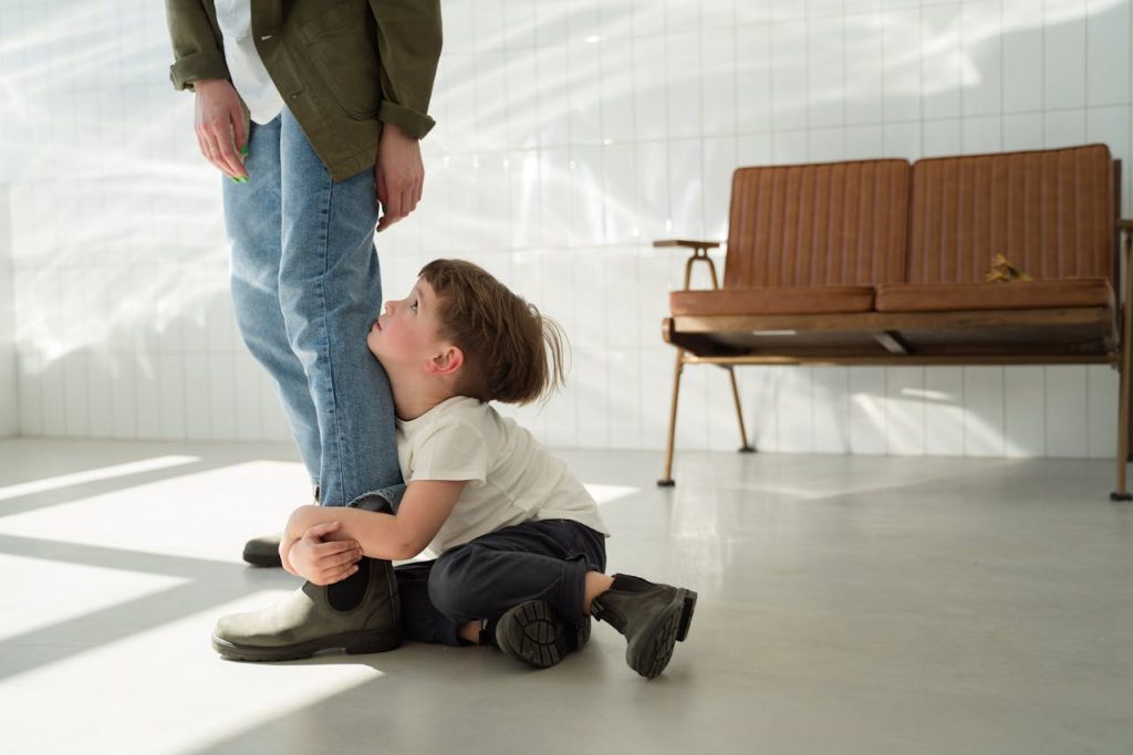 A young child clinging to a parent’s leg and looking up for approval, symbolizing the early roots of people-pleasing behavior.