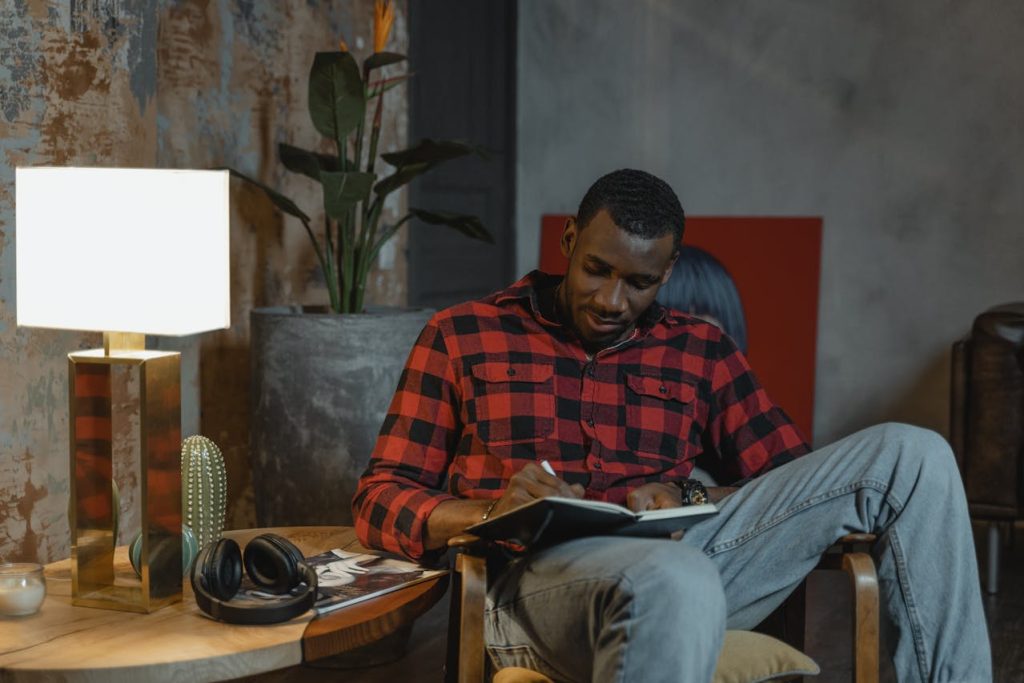 A man writing in his journal in a warm, cozy room, reflecting on his thoughts for self-discovery.