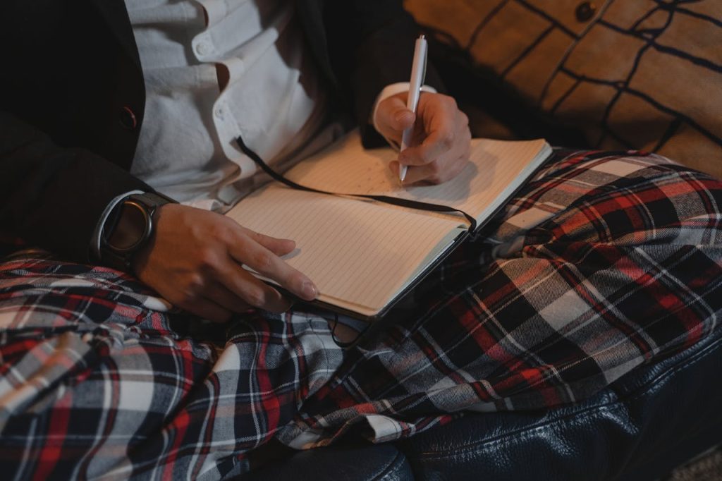 Close-up of a man writing in a leather-bound journal while sitting comfortably, symbolizing intentional self-reflection and personal growth.