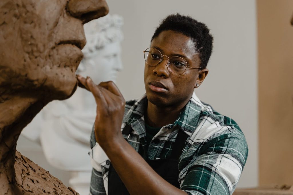 A man carefully sculpting a clay bust in a studio, illustrating creative outlets for men through focused, hands-on artistic expression.