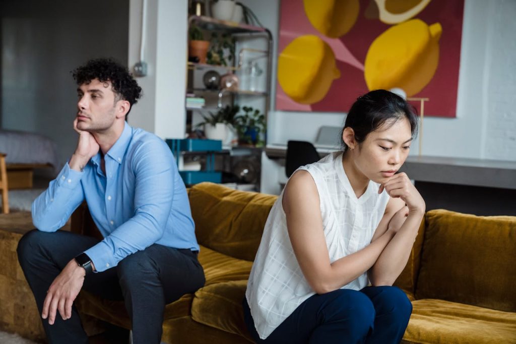 A couple sitting apart on a couch, both appearing emotionally distant, illustrating discomfort with intimacy associated with avoidant attachment in men.