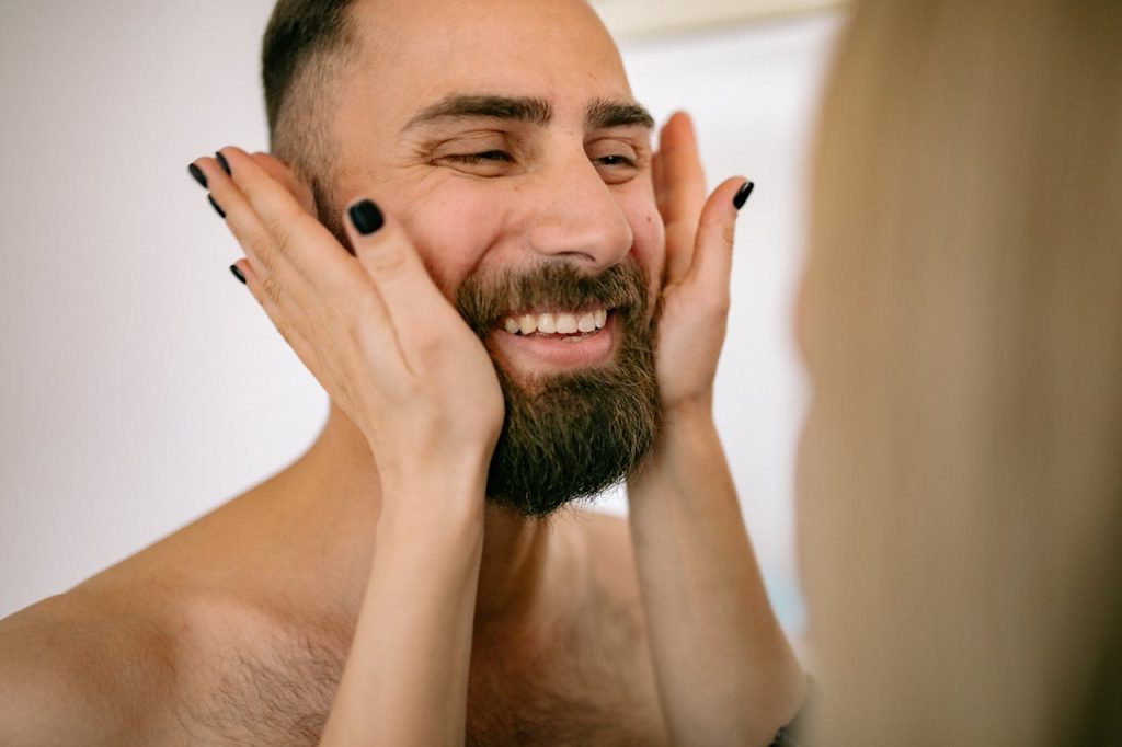 A smiling man being gently touched on the face, illustrating emotional intelligence in men through emotional awareness, connection, and positive expression.