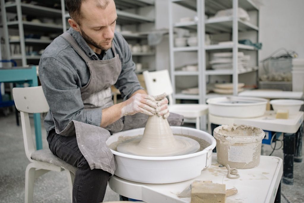A man shaping clay on a pottery wheel in a workshop, demonstrating creative outlets for men through hands-on craft and focused making.