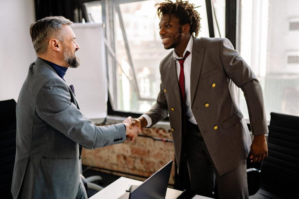 Two men in suits warmly shaking hands in an office, expressing sincere gratitude and mutual respect after receiving help.