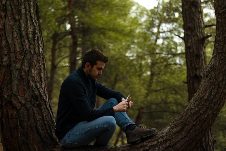 Man sitting alone on a tree branch in a forest, reflecting quietly, symbolizing the long-term emotional impact of growing up without a father.