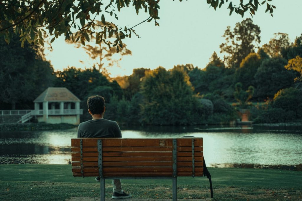 Man sitting alone on a park bench at sunset, calmly reflecting, symbolizing peaceful solitude and overcoming the fear of being alone.