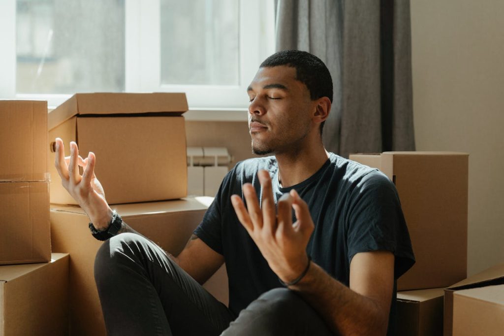 A man sitting calmly among moving boxes with eyes closed and hands open, practicing breathing for anger management and emotional regulation.