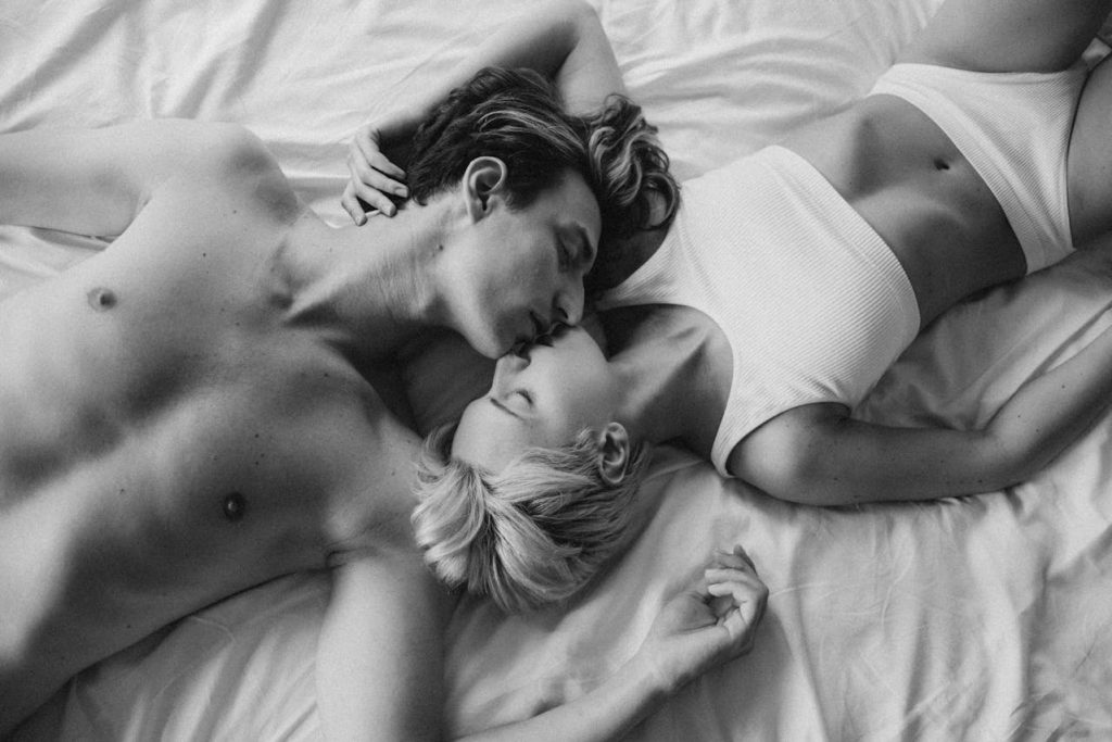 Couple lying close together and kissing softly in bed, expressing intimacy beyond sex through emotional closeness and trust.