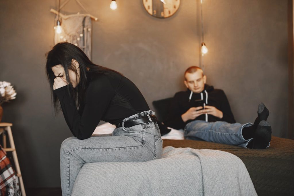 Man checking his phone while his partner sits nearby looking distressed, illustrating work intruding into personal and relationship time.