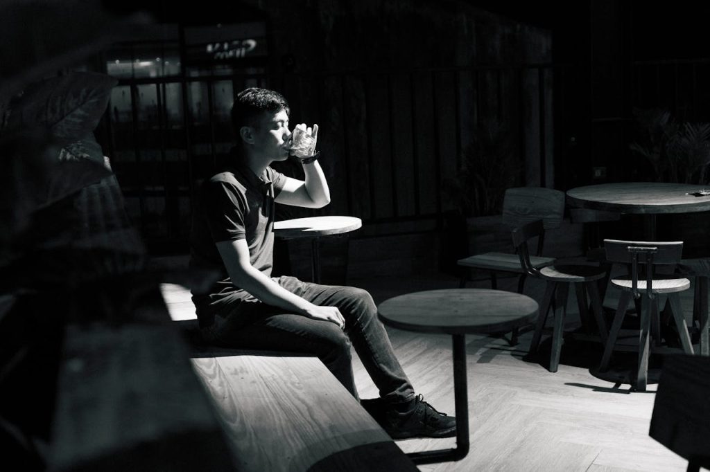Man sitting alone in a dimly lit room, drinking quietly, symbolizing isolation and suppressed emotions linked to toxic masculinity.