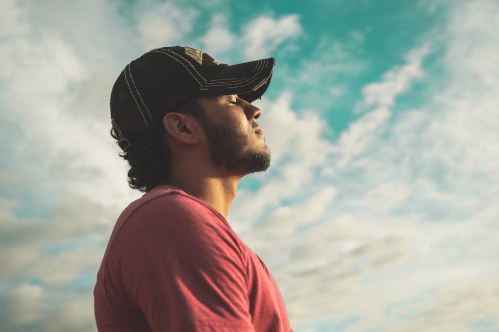 A man outdoors with eyes closed, taking a deep breath under an open sky, practicing calm breathing as a first step in anger management for men.