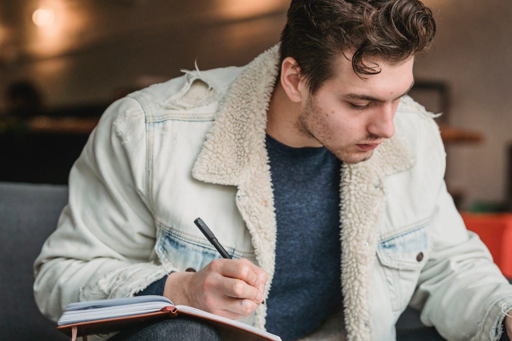 A young man writing thoughtfully in a notebook, illustrating self-reflection and intentional planning as healthy tools for anger management in men.