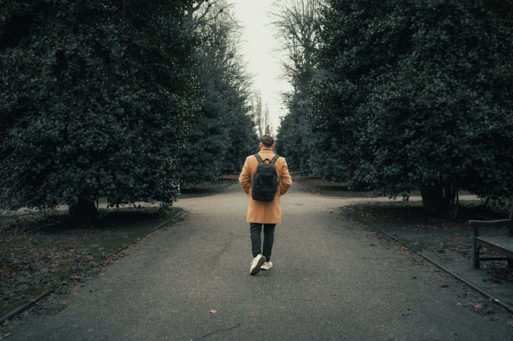 A man walking alone along a tree-lined path, appearing calm and reflective, illustrating the use of physical movement and nature as a healthy outlet for anger in men.