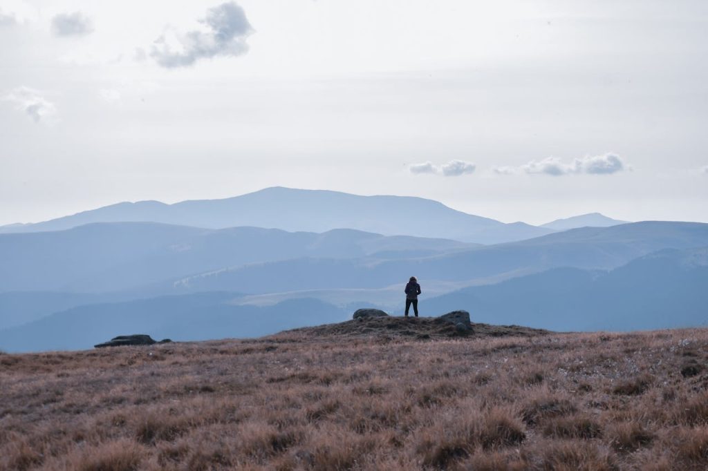 A man standing alone at the edge of a vast mountain landscape, facing the horizon, symbolizing authenticity over conformity and quiet self-trust.