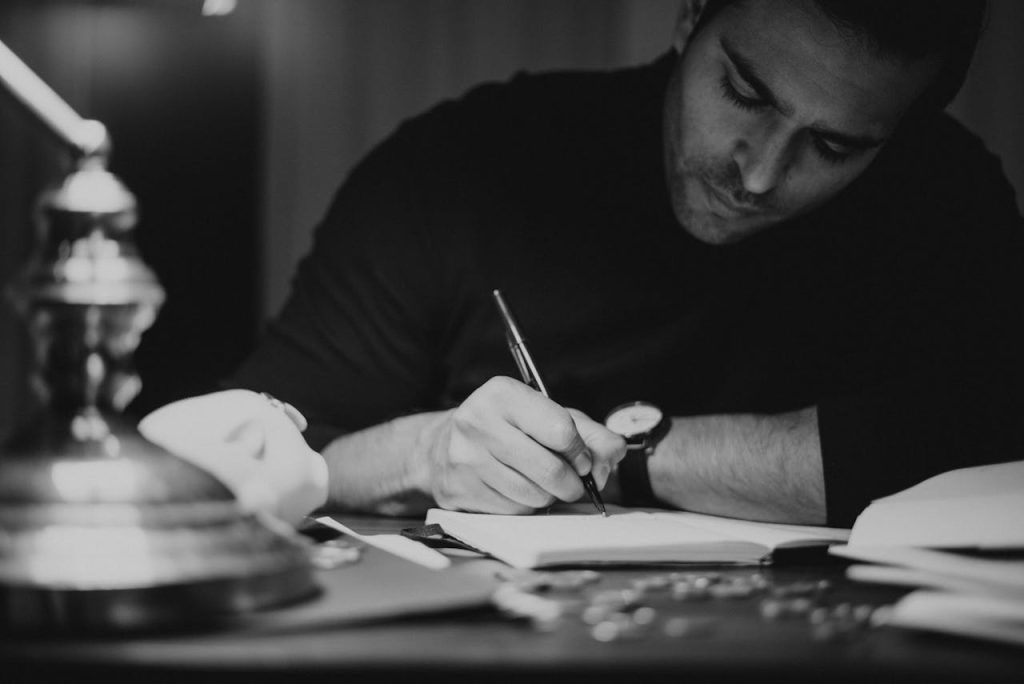 Man writing thoughtfully in a notebook at a desk, symbolizing imposter syndrome in men and the practice of documenting achievements to build self-trust.