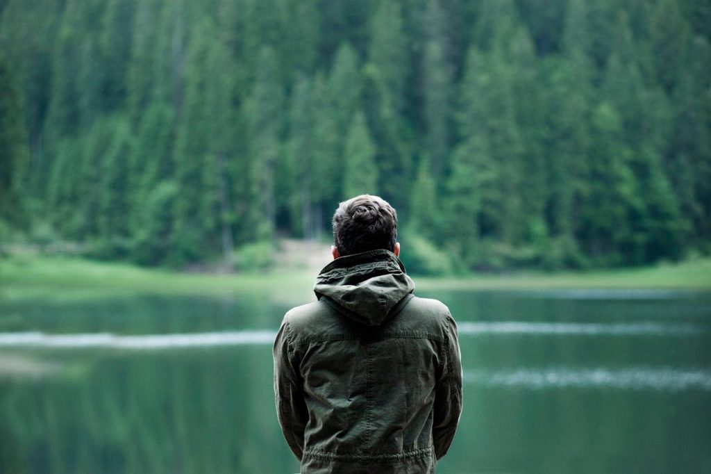 Man standing alone by a calm lake surrounded by forest, illustrating self-compassion for men through solitude, stillness, and self-acceptance.