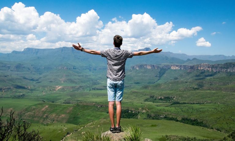A man standing on a mountain with arms open toward the horizon, illustrating finding inner peace through perspective, calm, and emotional release.