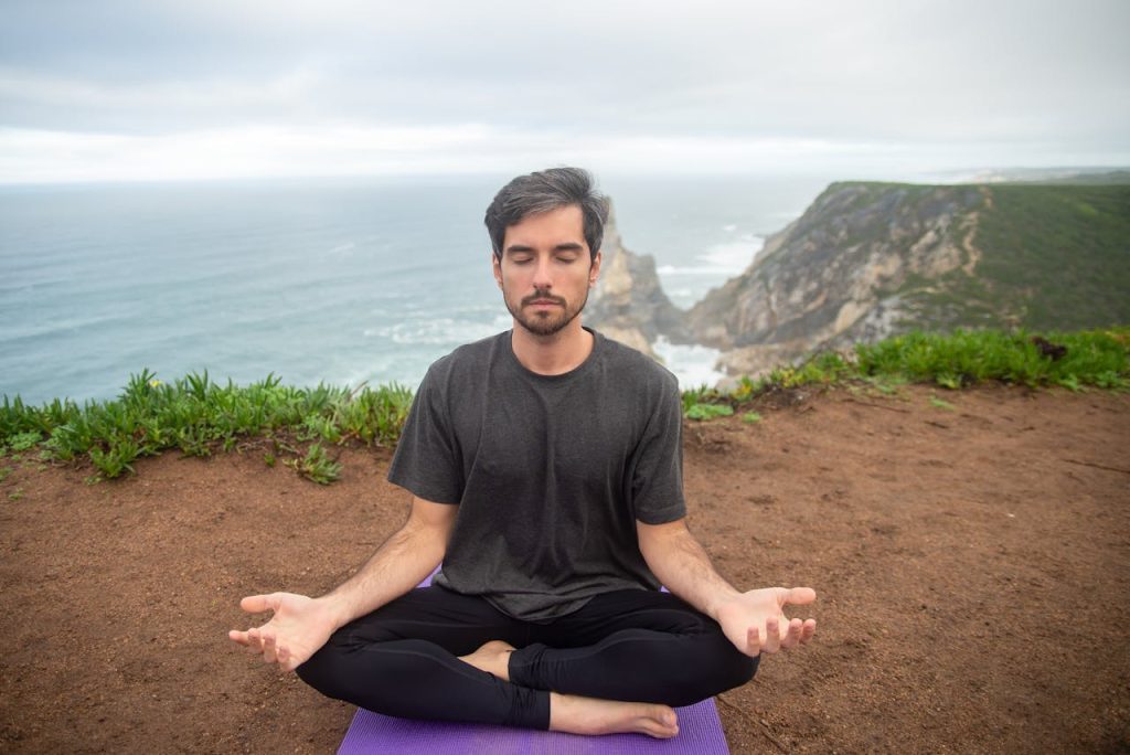 A man sitting cross-legged outdoors with eyes closed and hands resting on his knees, practicing breathwork and meditation to support finding inner peace.
