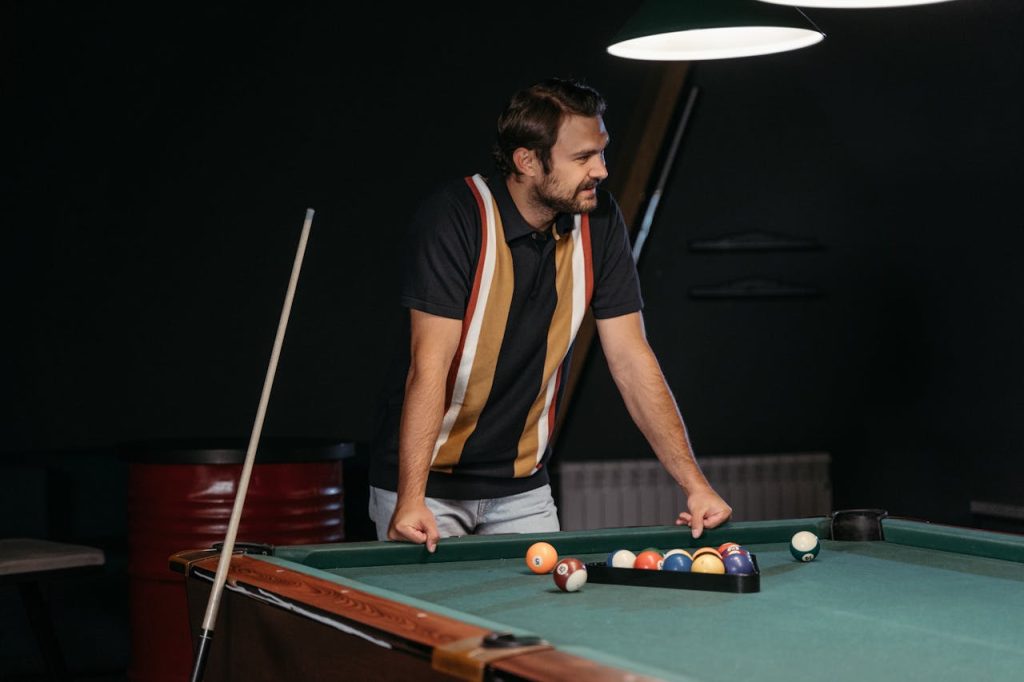 A man standing calmly beside a pool table with a relaxed posture and slight smile, illustrating humility as strength through quiet self-assurance rather than dominance.