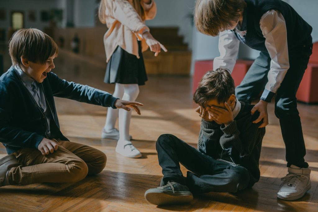 Young boy sitting on the floor covering his face while other children point at him, illustrating early experiences linked to overcoming shame as a man.