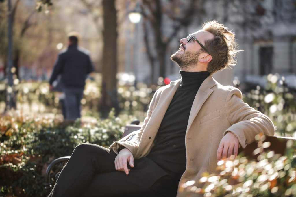 A man sitting peacefully outdoors on a bench, smiling and relaxed, illustrating redefining success for men through inner contentment rather than external achievement.