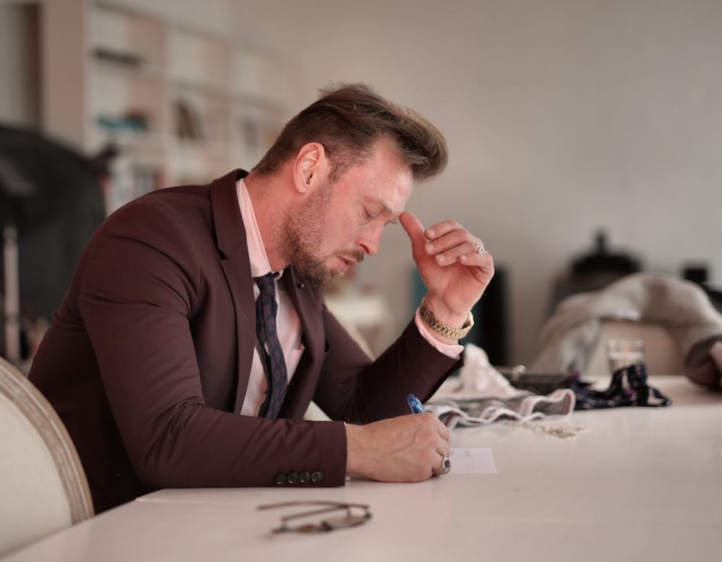 Businessman in a suit sitting at a desk with a tense expression, illustrating imposter syndrome in men and hidden self-doubt in professional settings.