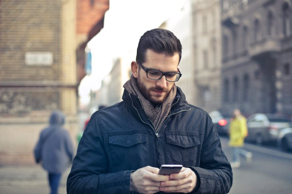 A man standing outdoors looking at his phone with a focused, self-assured expression, illustrating the contrast between self-promotion and humility as strength in men.