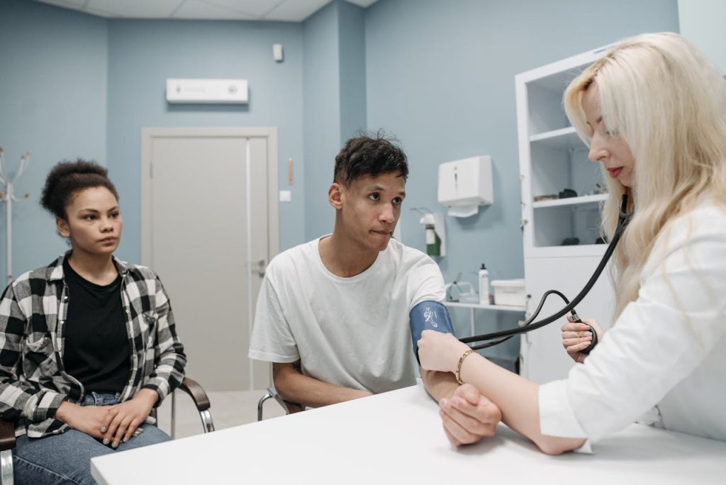 A man seated in a medical setting during a health check, appearing tense and uncomfortable, illustrating the physical symptoms often associated with depression in men.