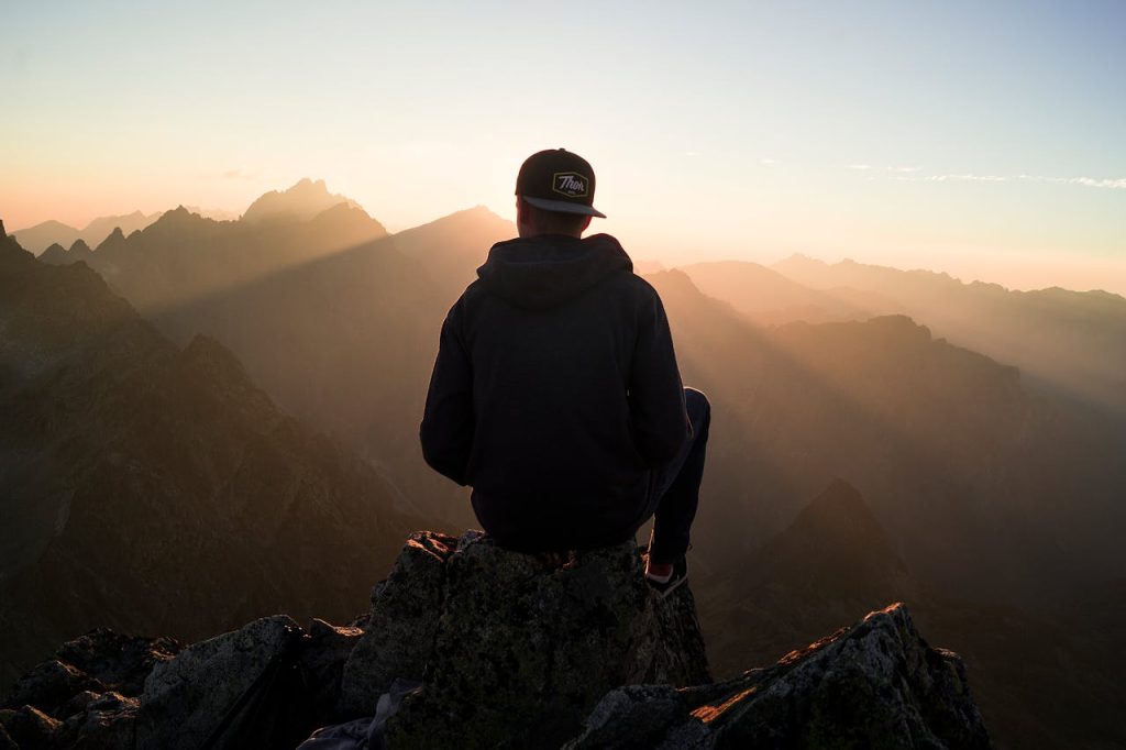 Man sitting alone on a mountain peak at sunrise, reflecting quietly, symbolizing imposter syndrome in men and the journey from self-doubt to self-trust.