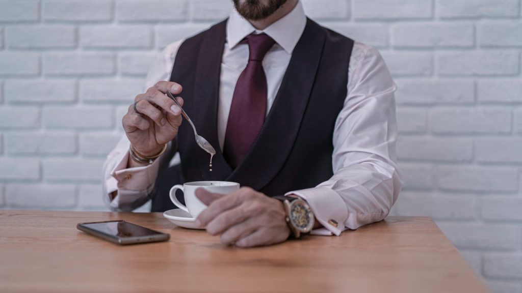 A man in formal attire placing his phone face-down beside a cup of coffee, symbolizing intentional disconnection and finding inner peace through presence.