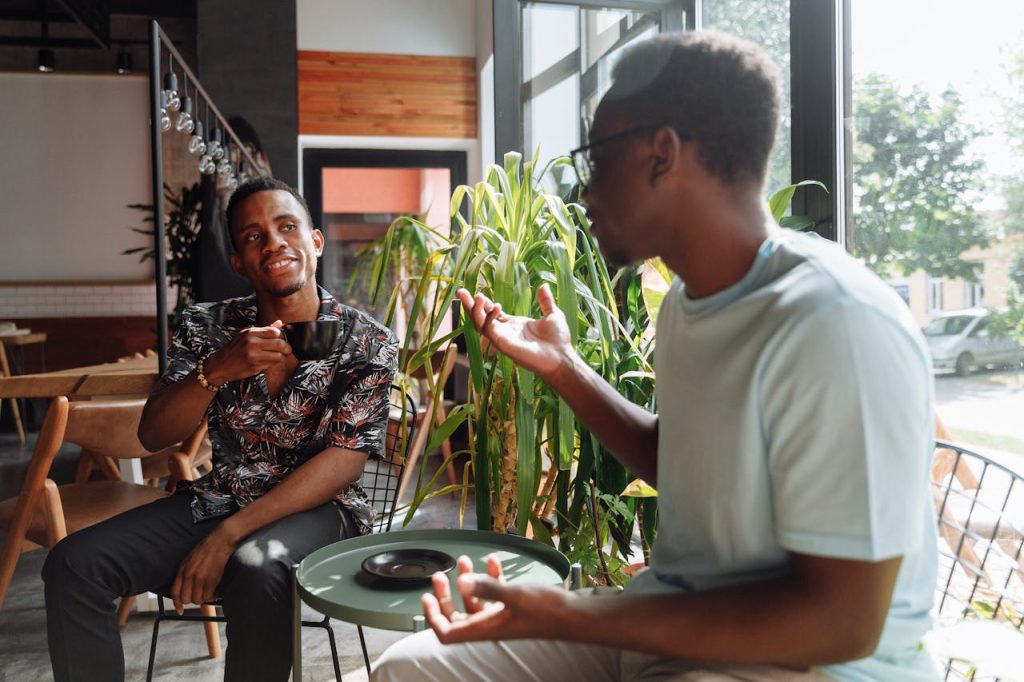 Two men sitting at a café having coffee, relaxed and engaged in conversation, illustrating humility as strength through mutual respect and genuine connection.