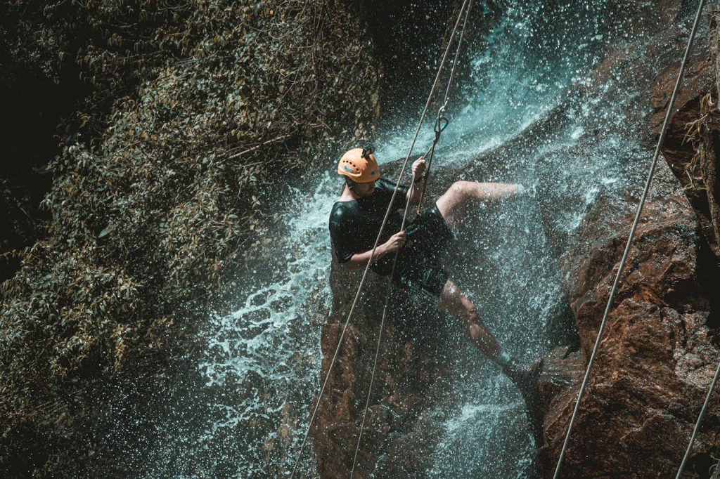 Man rappelling down a waterfall on a rocky cliff, symbolizing fear of failure in men and the courage to move forward despite risk.