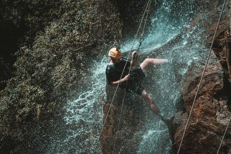 Man rappelling down a waterfall on a rocky cliff, symbolizing fear of failure in men and the courage to move forward despite risk.